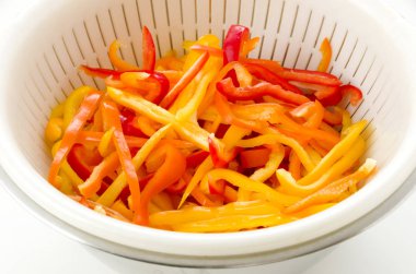 Beyaz arka planda kırmızı, turuncu ve sarı dolma biber beyaz plastik kolander 