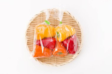 Beyaz arka planda bambu kevgir üzerinde plastik poşette taze renkli dolma biber.