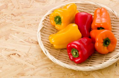 Osb kontrplak arka planında bambu süzgecinde taze renkli dolma biber.