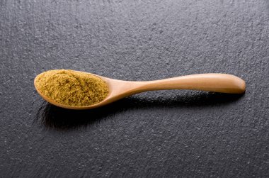 Siyah taş tabakta tahta kaşıkta kimyon tozu.