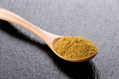 Siyah taş tabakta tahta kaşıkta kimyon tozu.