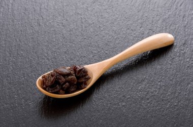 Kuru üzümler siyah taş arka planda tahta bir kaşıkta