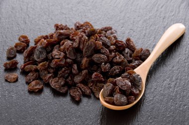 Kuru üzümler siyah taş arka planda tahta kaşıkta