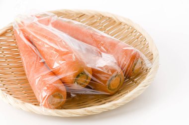 Beyaz arka planda bambu kevgire plastik poşet içinde taze havuç.