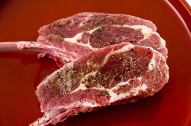 Kırmızı tepside beyaz arka planda çiğ kuzu pirzolası 