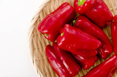 Beyaz arka planda kırmızı dolma biber ve bambu kevgir.