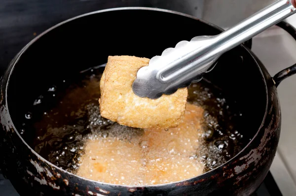Deep frying tofu in boil oil, Tongs holding Deep frying thick fried tofu.