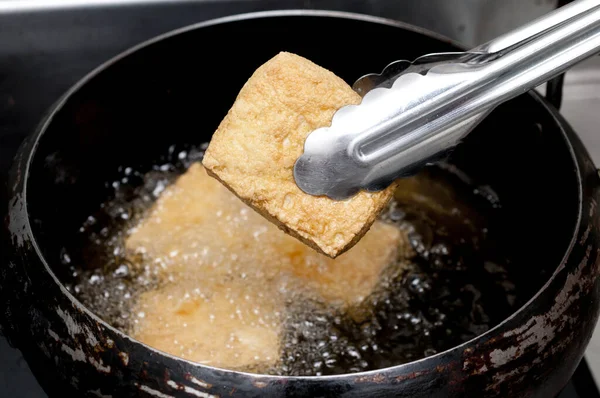 Deep frying tofu in boil oil, Tongs holding Deep frying thick fried tofu.