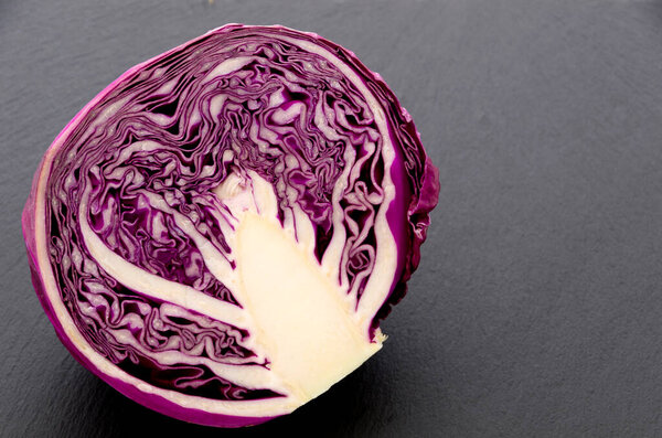 Sliced purple cabbage isolated on black stone plate