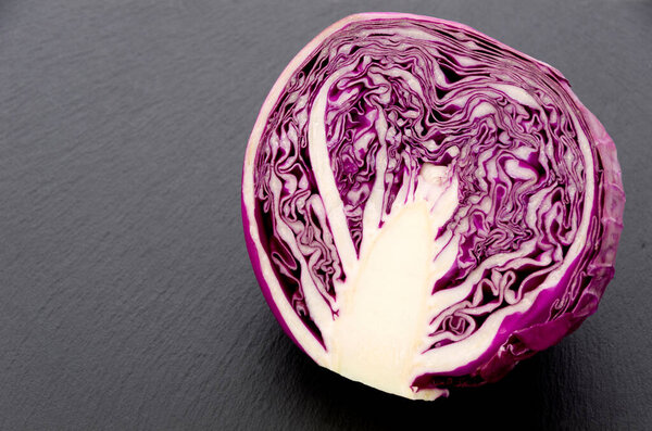 Sliced purple cabbage isolated on black stone plate