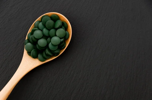 Zielone Tabletki Spirulina Tabletki Drewnianej Łyżce Czarnej Kamiennej Płytce — Zdjęcie stockowe