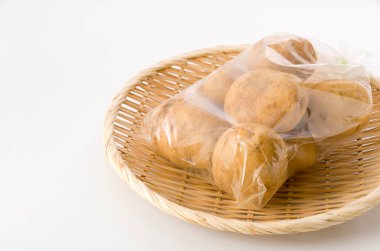 Beyaz arka planda bambu süzgeci üzerinde plastik poşette patates