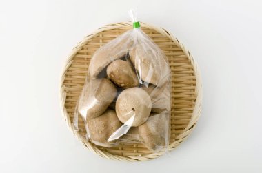 Shiitake mantarı şeffaf plastik torba içinde beyaz arka planda bambu kevgir.
