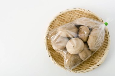 Shiitake mantarı şeffaf plastik torba içinde beyaz arka planda bambu kevgir.