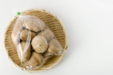 Shiitake mantarı şeffaf plastik torba içinde beyaz arka planda bambu kevgir.