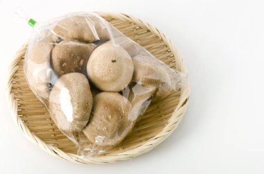 Shiitake mantarı şeffaf plastik torba içinde beyaz arka planda bambu kevgir.