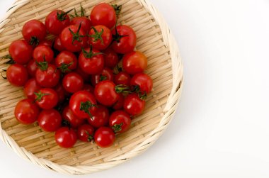 Beyaz arka planda bambu kevgire bulanmış taze kırmızı kiraz domatesleri.