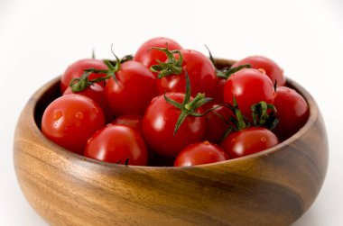 Beyaz arka planda ahşap yuvarlak kasede taze kırmızı kiraz domatesleri.