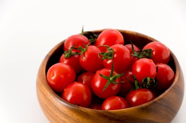 Beyaz arka planda ahşap yuvarlak kasede taze kırmızı kiraz domatesleri.