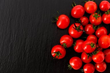 Siyah taş tabakta taze kırmızı kiraz domatesleri.