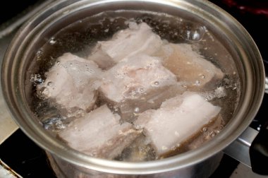 Gaz ocağında paslanmaz çelik tencereyle kaynayan suda domuz eti. 