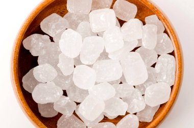 Yuvarlak ahşap bir kasede beyaz arka planda beyaz kaya şekeri