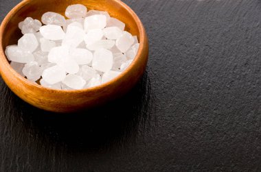 Yuvarlak ahşap bir kasede siyah taş tabakta beyaz kaya şekeri.