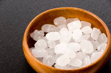 Yuvarlak ahşap bir kasede siyah taş tabakta beyaz kaya şekeri.