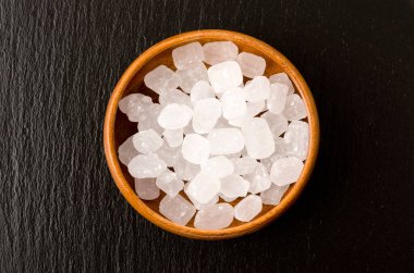 Yuvarlak ahşap bir kasede siyah taş tabakta beyaz kaya şekeri.