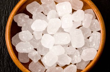 Yuvarlak ahşap bir kasede siyah taş tabakta beyaz kaya şekeri.