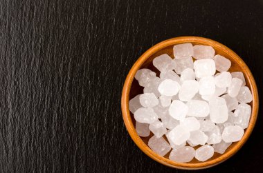 Yuvarlak ahşap bir kasede siyah taş tabakta beyaz kaya şekeri.