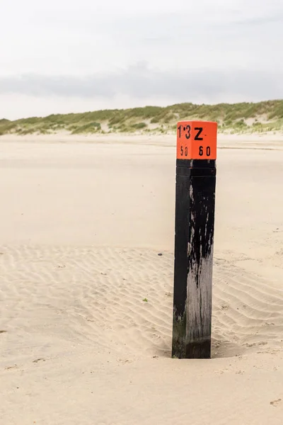 A wooden black pole with red head stands on the beach at the Nor