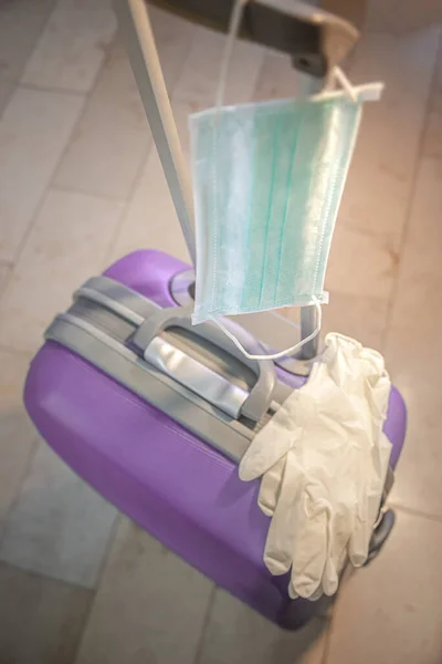Medical face mask is hanging on travel violet suitcase and medic — Stock Photo, Image