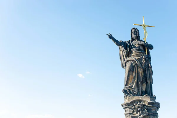 Ancient statue of a saint monk with a cross at the Charles Bridge in Prague at blue sky and copy space, Czech Republic, summer