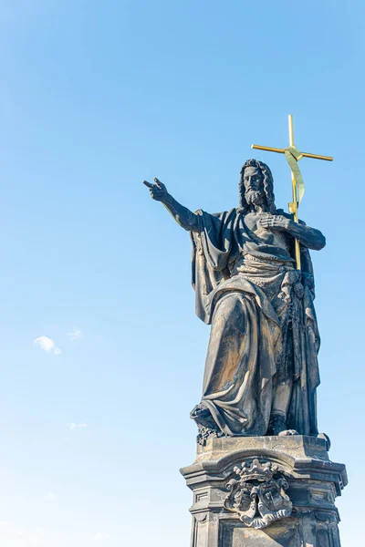 Ancient statue of a saint monk with a cross at the Charles Bridge in Prague at blue sky and copy space, Czech Republic, summer