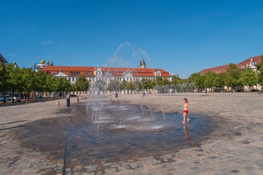 Büyük Katedral Meydanı (Domplatz), çocuklar güneşli bir günde ve mavi gökyüzünde Magdeburg 'da Katedral ve Hükümet Ofisi' nin yanındaki çeşmelerde oynuyorlar.