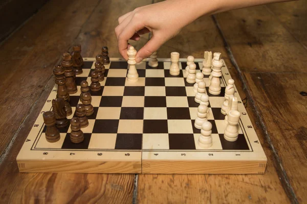 Uma única mão jogando xadrez em um tabuleiro de madeira definido em alguma madeira — Fotografia de Stock
