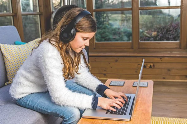 Teenage girl on laptop with headphone in the conservatory