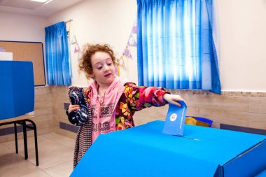 Cute redhead little girl is trusted by her parent to put their vote envelope in the box. (Israeli elections) clipart
