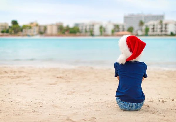 Küçük kız sahilde oturuyor. Noel ve yeni yıl tatilleri kavramı. — Stok fotoğraf