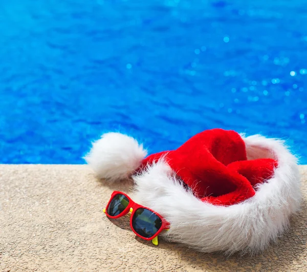 Piros karácsonyi kalap és napszemüveg közelében a medence. Hely a szöveg. — Stock Fotó