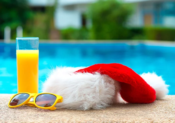 Karácsonyi kalapot, napszemüveget és narancslé a medence közelében. — Stock Fotó