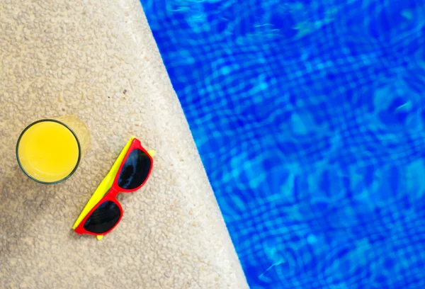 Jugo de naranja y gafas de sol cerca de la piscina. Espacio para texto . — Foto de Stock