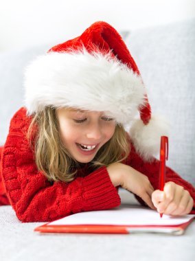 Noel Baba'ya bir mektup yazma kırmızı şapkalı mutlu küçük kız.