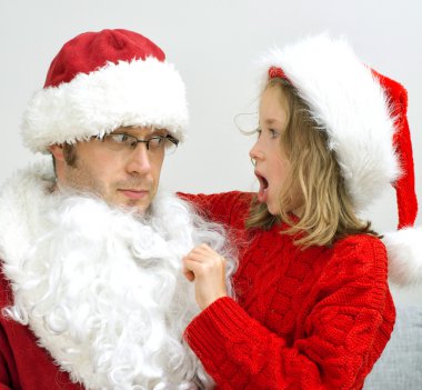 Surprised little girl looking at fake Santa Claus. clipart