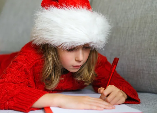Petite fille au chapeau rouge écrivant une lettre au Père Noël . — Photo