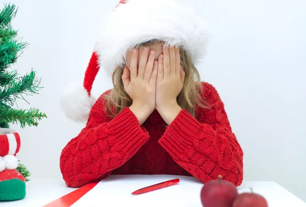 Kırmızı şapka Noel Baba'ya bir mektup yazma, üzgün küçük kız. — Stok fotoğraf