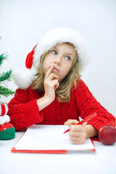 Noel Baba'ya bir mektup yazma kırmızı şapkalı küçük kız. — Stok fotoğraf