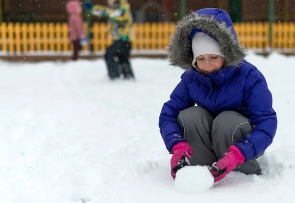 Liten flicka rullande snöboll i vinter. — Stockfoto