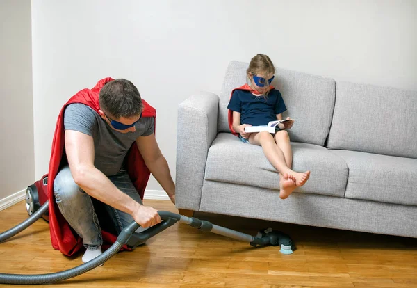 Ordinary day of superhero family. Dad vacuuming, daughter reading a book. — Stock Photo, Image